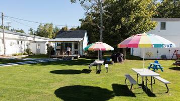 A backyard with a picnic table, two colorful umbrellas, and a small building.