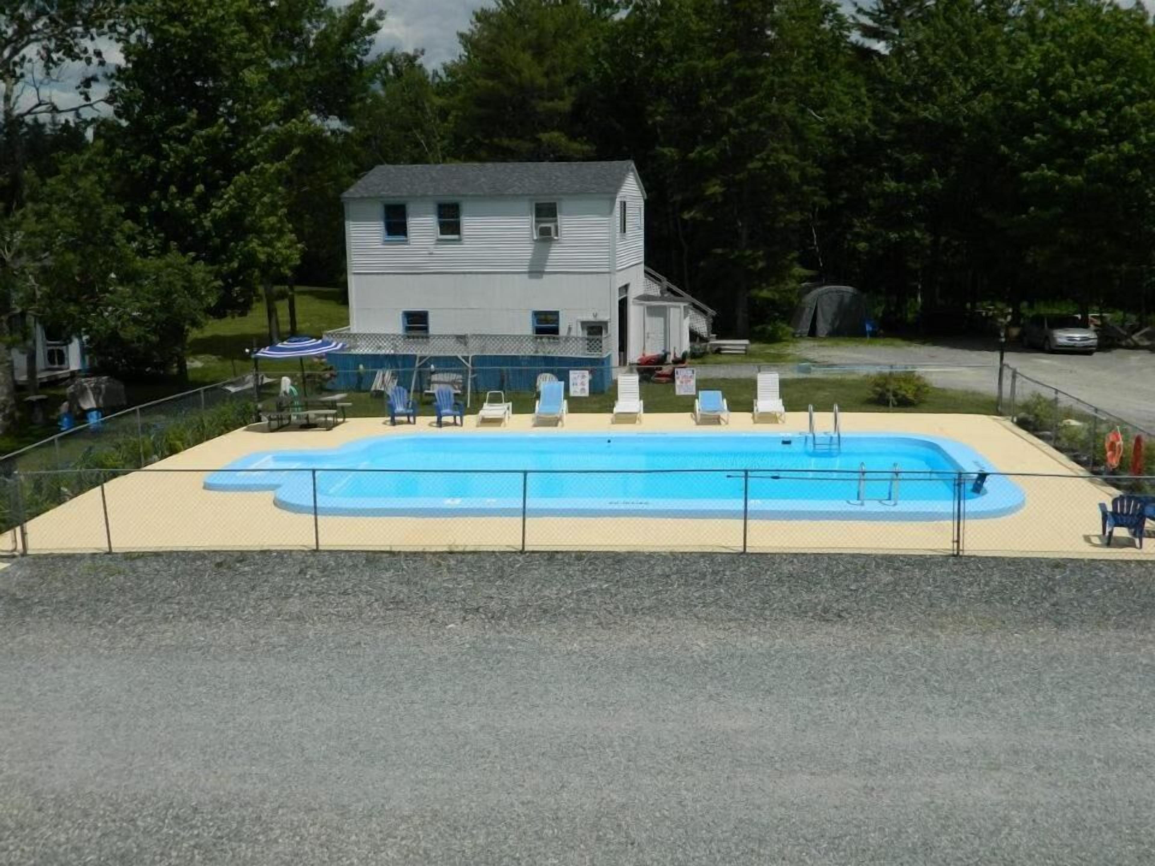 Una piscina con sillas de descanso, un área cercada y un edificio al fondo.