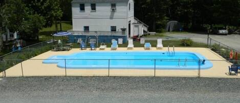 Una piscina con sillas de descanso, un área cercada y un edificio al fondo.