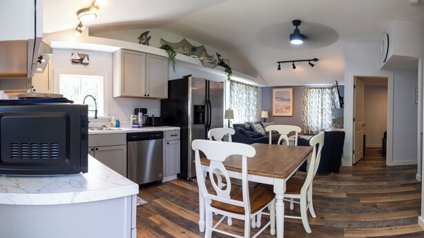 A compact kitchen with modern appliances, a dining area with white chairs, and a hallway leading to a bedroom. - 3BedroomApt Pool CampFire PlayArea (Bar Harbor)