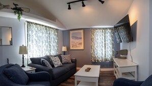 A modern living room with a grey sofa, a white coffee table, and a TV mounted on the wall. - 3BedroomApt Pool CampFire PlayArea (Bar Harbor)
