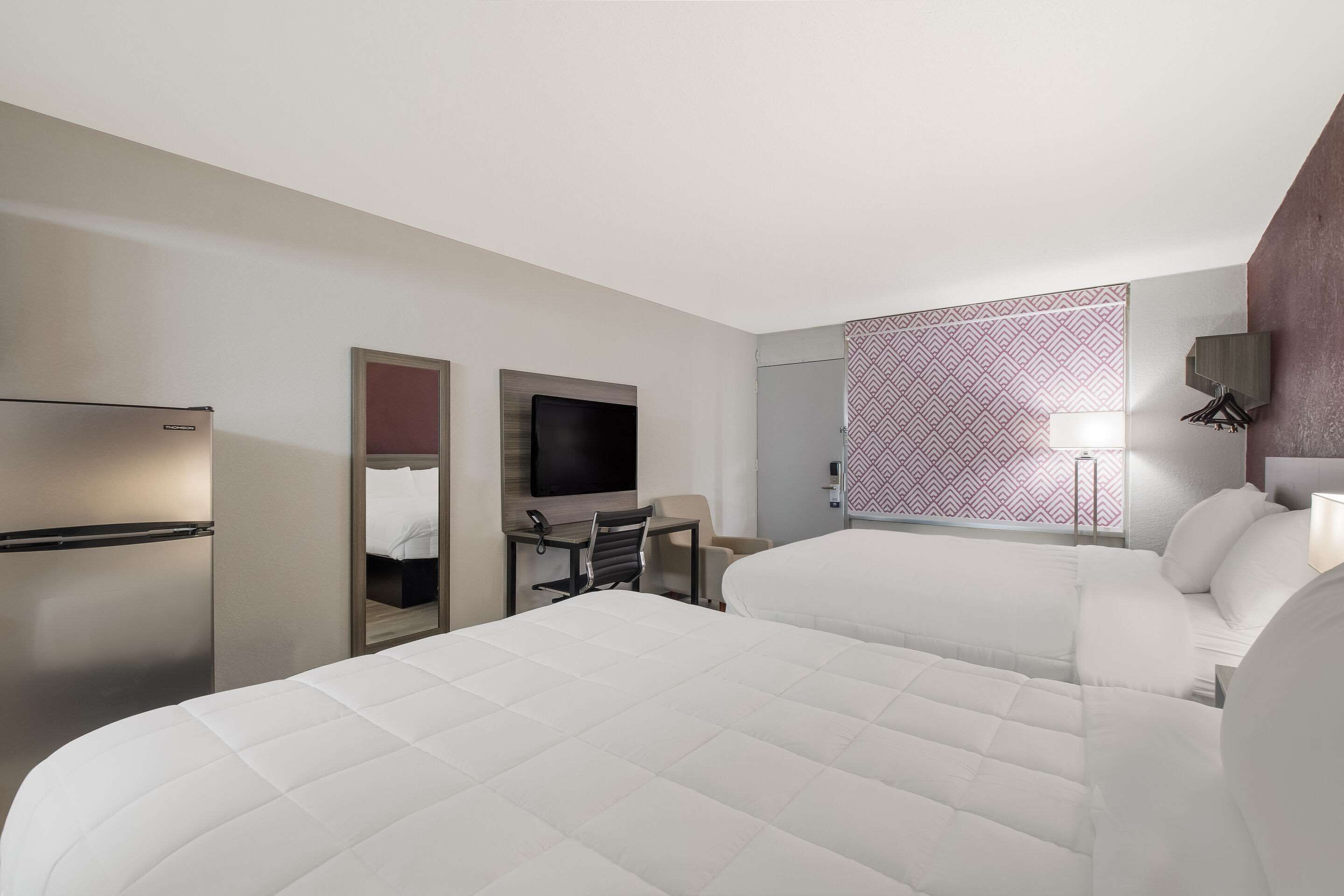 Ein Hotelzimmer mit einem großen Bett, einem Schreibtisch mit Stuhl, einem Fernseher und einer Minibar.
