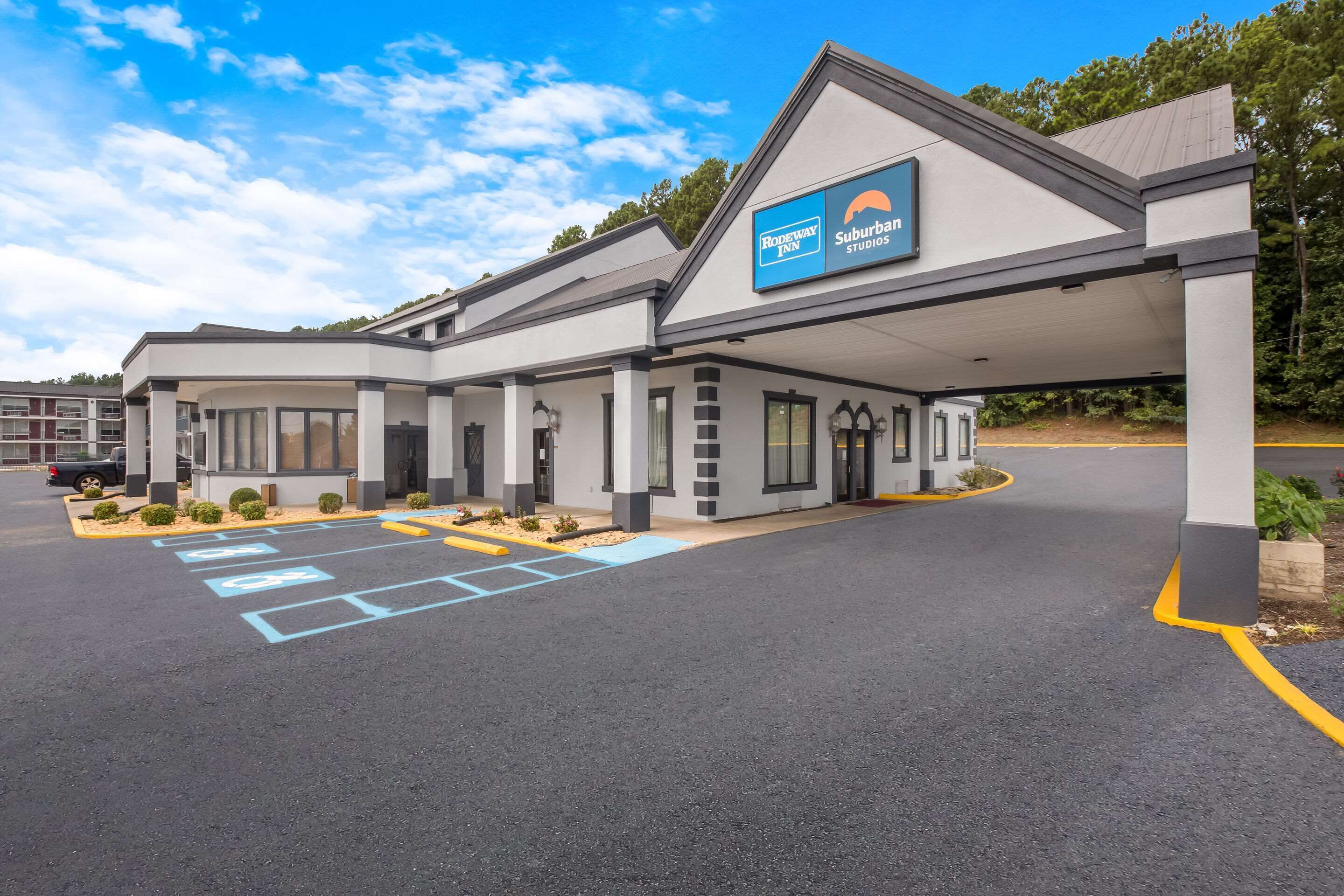 A modern hotel with a covered entrance, marked parking spaces, and a sign for 'Rodeway Inn Suburban Studios'.