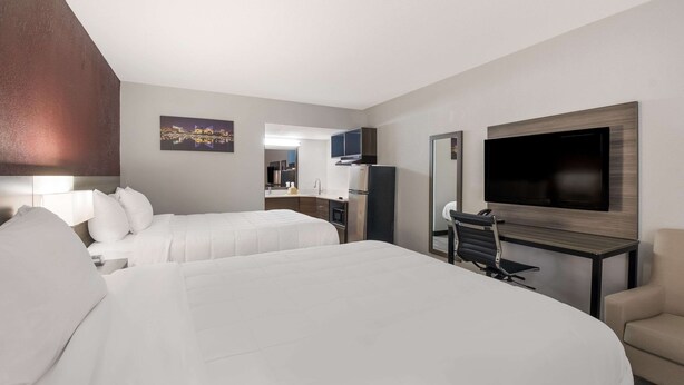 Ein Hotelzimmer mit zwei Betten, einem Schreibtisch mit Stuhl, einem Fernseher und einem Spiegel.