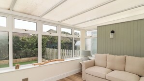 A room with a wooden floor, a beige sofa, and a window with a view of a garden. - Gudhjem (Seahouses)