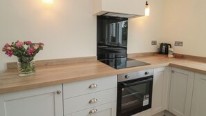 A modern kitchen with a black stove, white cabinets, and a wooden countertop. There are two wall-mounted lights and a vase with flowers on the counter. - Gudhjem (Seahouses)