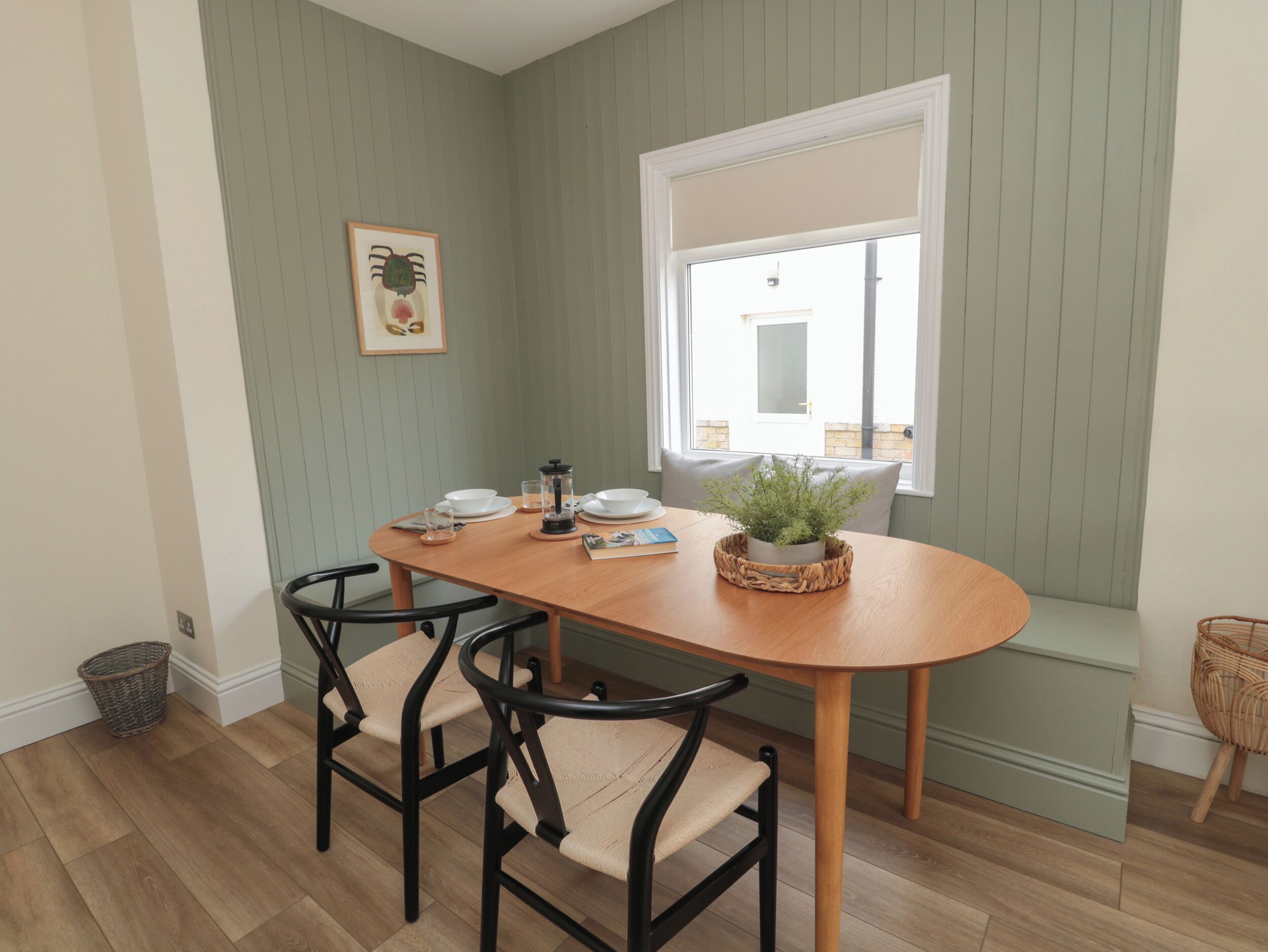 A dining area with a wooden table, two chairs, a window with a view, and a framed picture on the wall.
