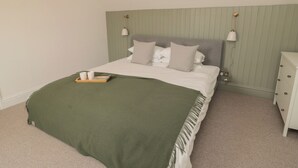 A neatly made bed with a green throw blanket, two bedside lamps, and a bedside table with a tray of items. - Gudhjem (Seahouses)