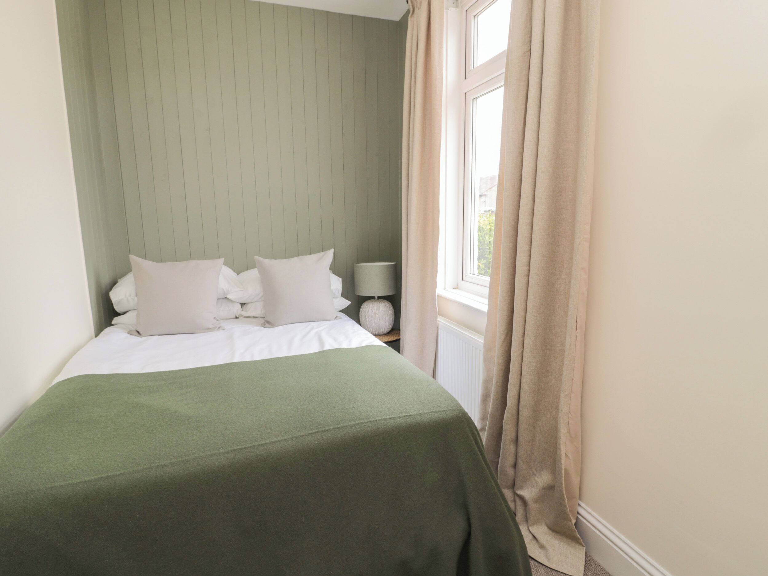Un lit bien fait, avec une couvre-lit verte, des oreillers blancs et une tête de lit ornée de panneaux verticaux.
