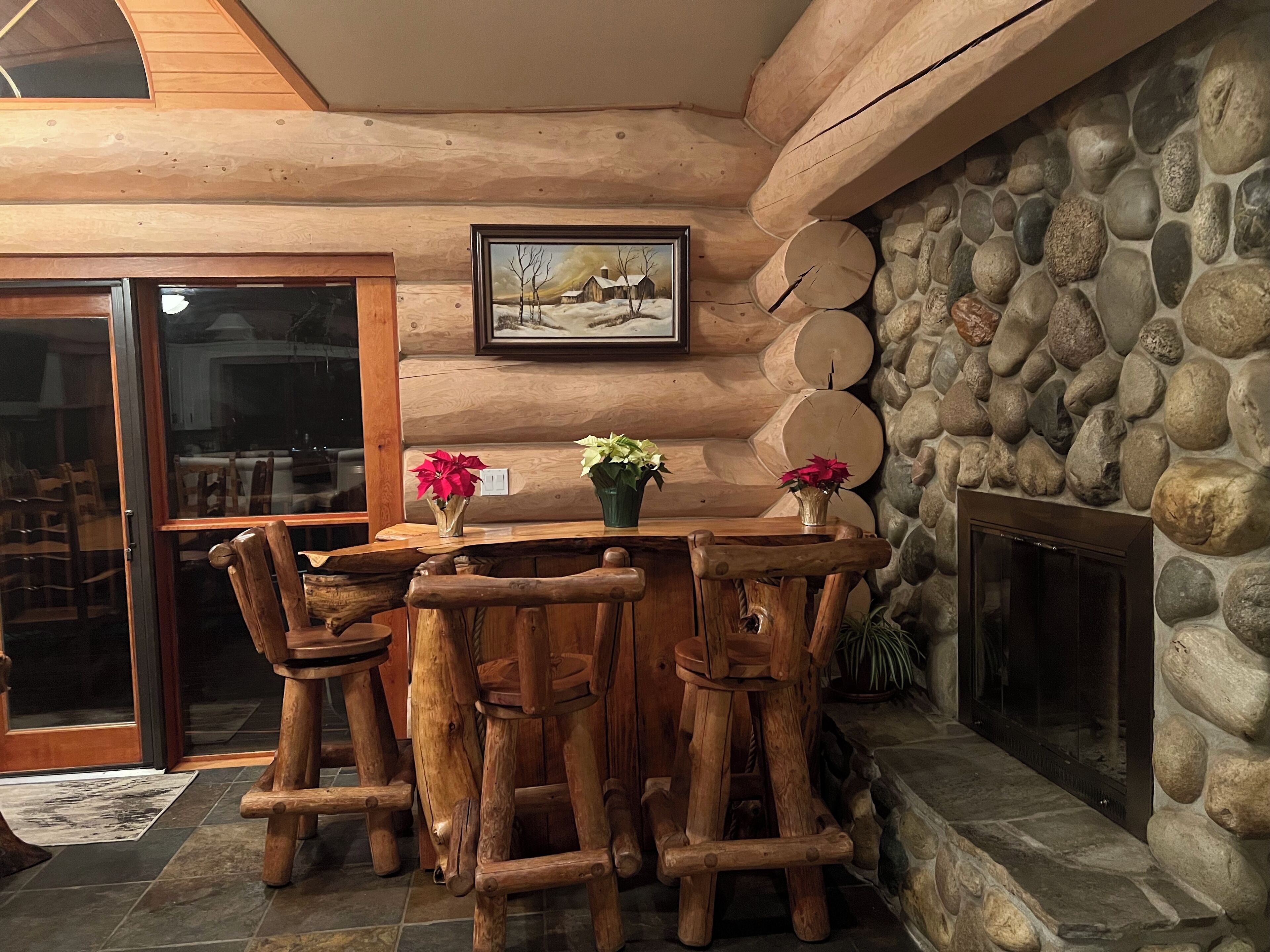 A rustic wooden dining area with a stone fireplace, wooden chairs, and a table with potted plants.