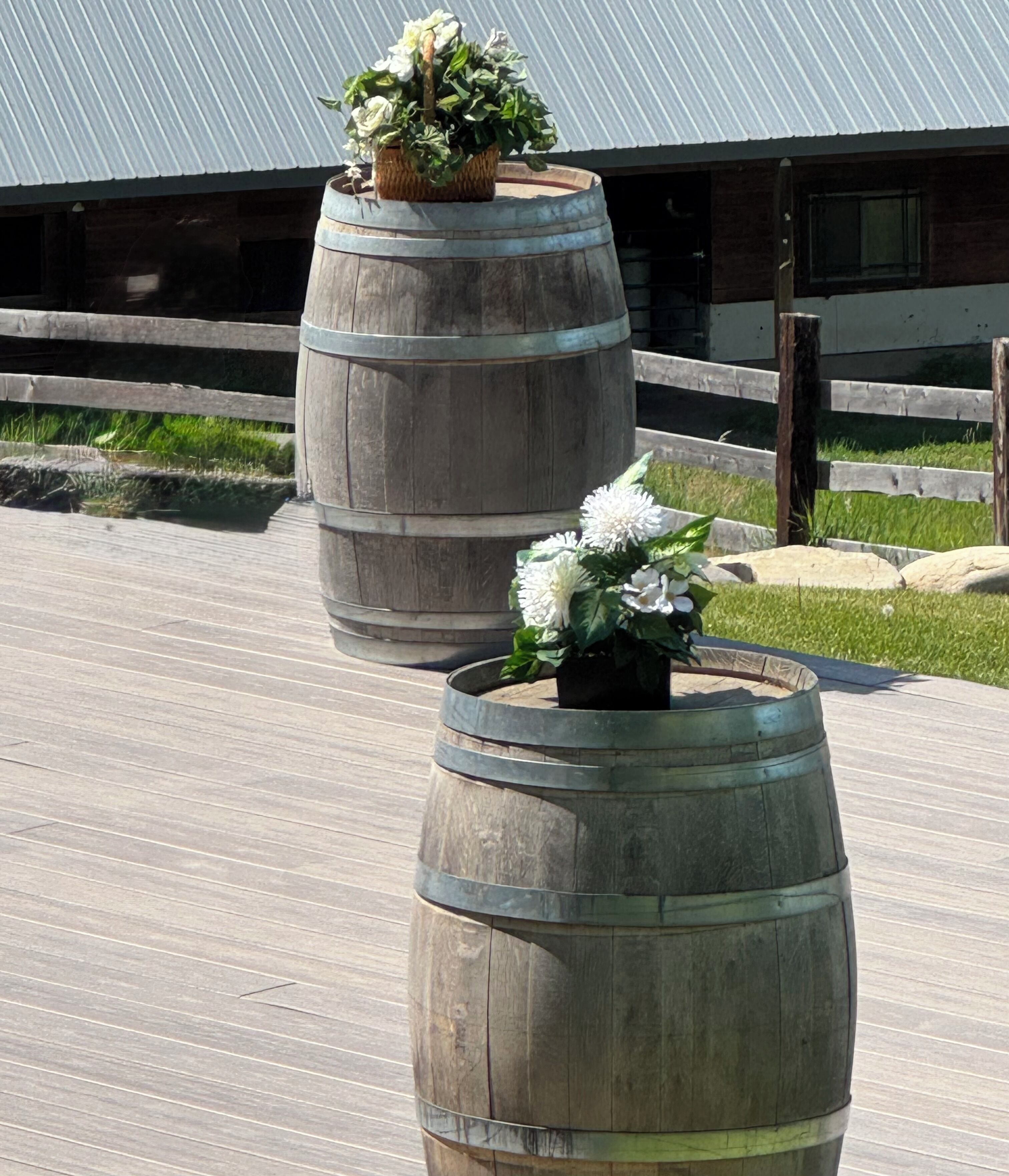Two wooden barrels used as planters with flowers, placed on a wooden deck.