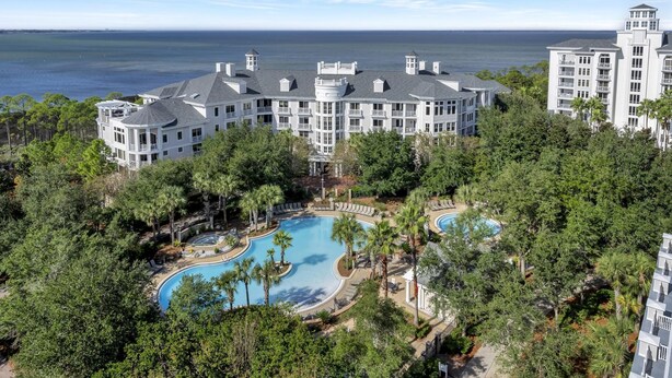 A large resort with multiple swimming pools surrounded by lush greenery and a view of the ocean.