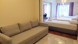 Quarto de hotel com sofá, duas camas, porta que dá para uma varanda e vista para o exterior.