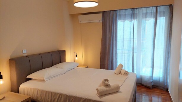 Quarto de hotel com uma cama, mesa de cabeceira, aparelho de ar condicionado e uma janela com cortinas.
