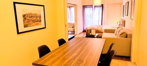 Quarto de hotel com uma mesa de jantar de madeira, um sofá, uma cama e um quadro na parede.