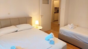 Een hotelkamer met twee bedden, een nachtkastje met een lamp, en uitzicht op de keuken door een geopende deur.