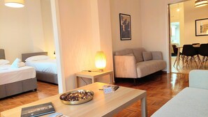 A hotel room with two beds, a sofa, a dining area, and a table with a bowl of nuts. - Big Apartment in Acropolis Museum (Athens)