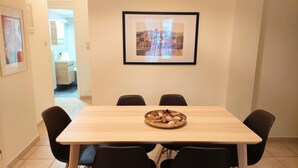 A dining area with a wooden table and four chairs, a framed picture on the wall, and a bowl of food on the table. - Big Apartment in Acropolis Museum (Athens)