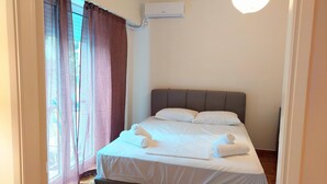 A neatly made bed with white linens and towels, a grey headboard, and an air conditioning unit on the wall. - Big Apartment in Acropolis Museum (Athens)