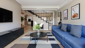 A modern living room with a blue sofa, a black coffee table with a vase, a flat-screen TV, and a staircase leading to another room. - Wynwood House Nuevo Leon (Mexico City)