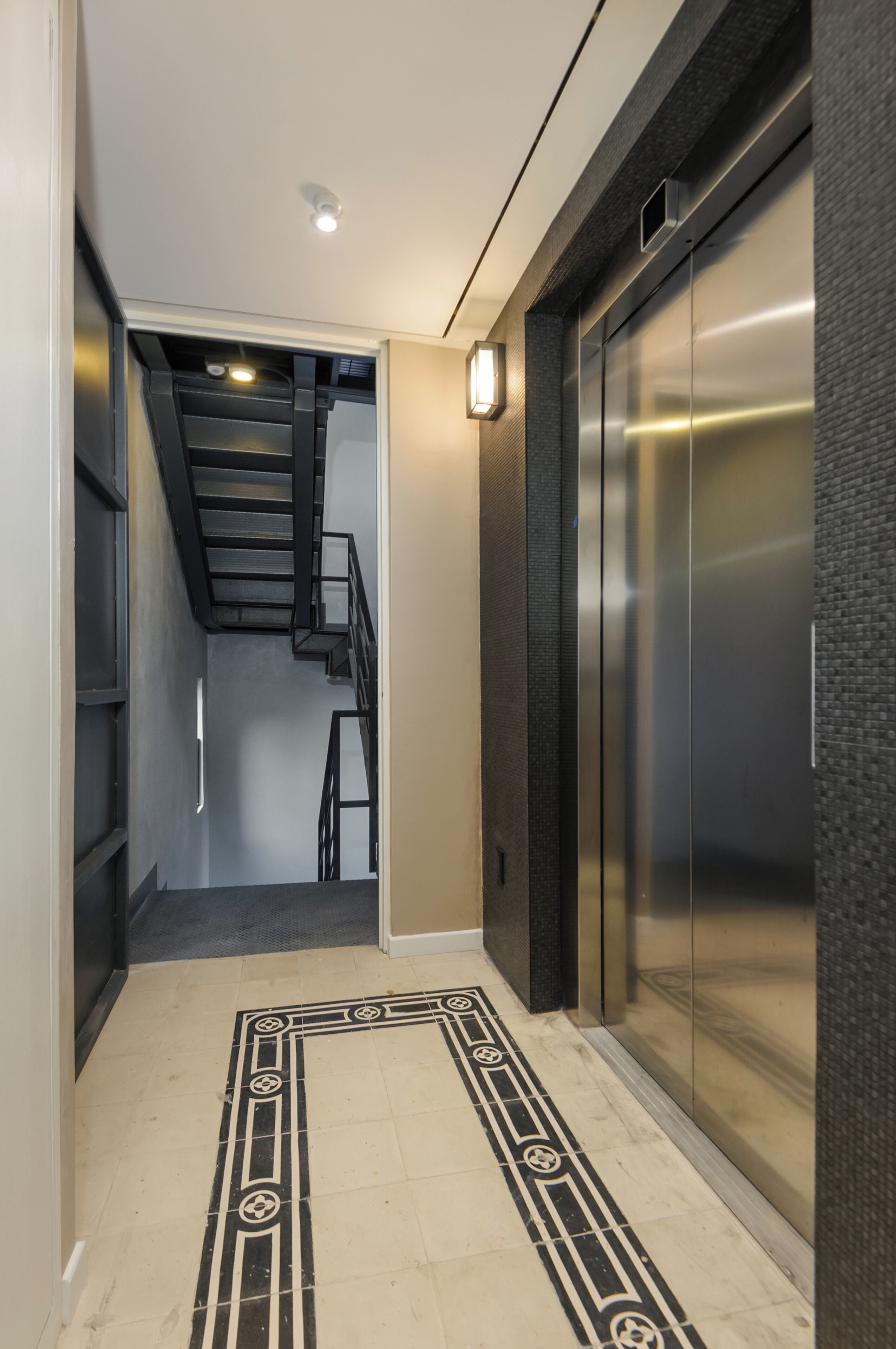 A hallway with a patterned floor, an elevator, and a staircase.