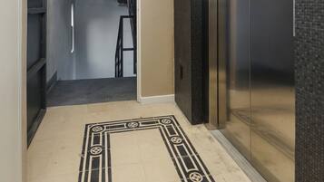 A hallway with a patterned floor, an elevator, and a staircase.