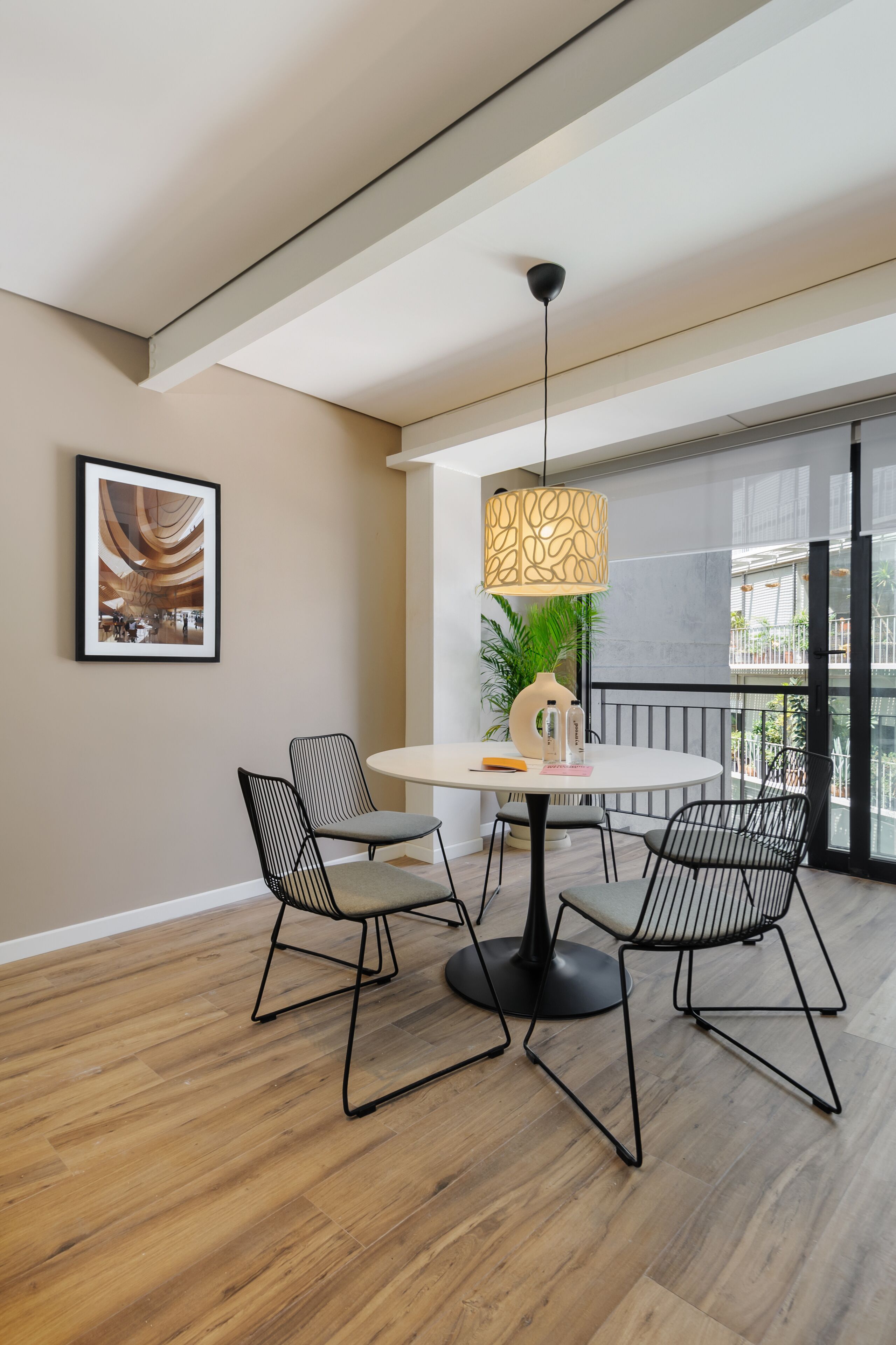 A modern dining area with a round table, two chairs, a pendant light, and a framed picture on the wall.