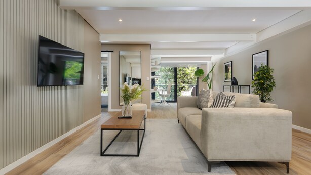A modern living room with a flat-screen TV mounted on the wall, a beige sofa, a coffee table, and a large mirror. - Wynwood House Nuevo Leon (Mexico City)