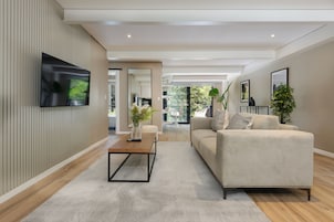 Un salon moderne avec un téléviseur à écran plat fixé au mur, un canapé beige, une table basse et un grand miroir.