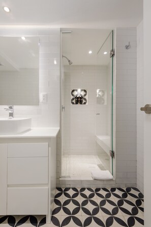 A modern bathroom with a glass-enclosed shower, white tiled walls, and a patterned floor. - Wynwood House Nuevo Leon (Mexico City)