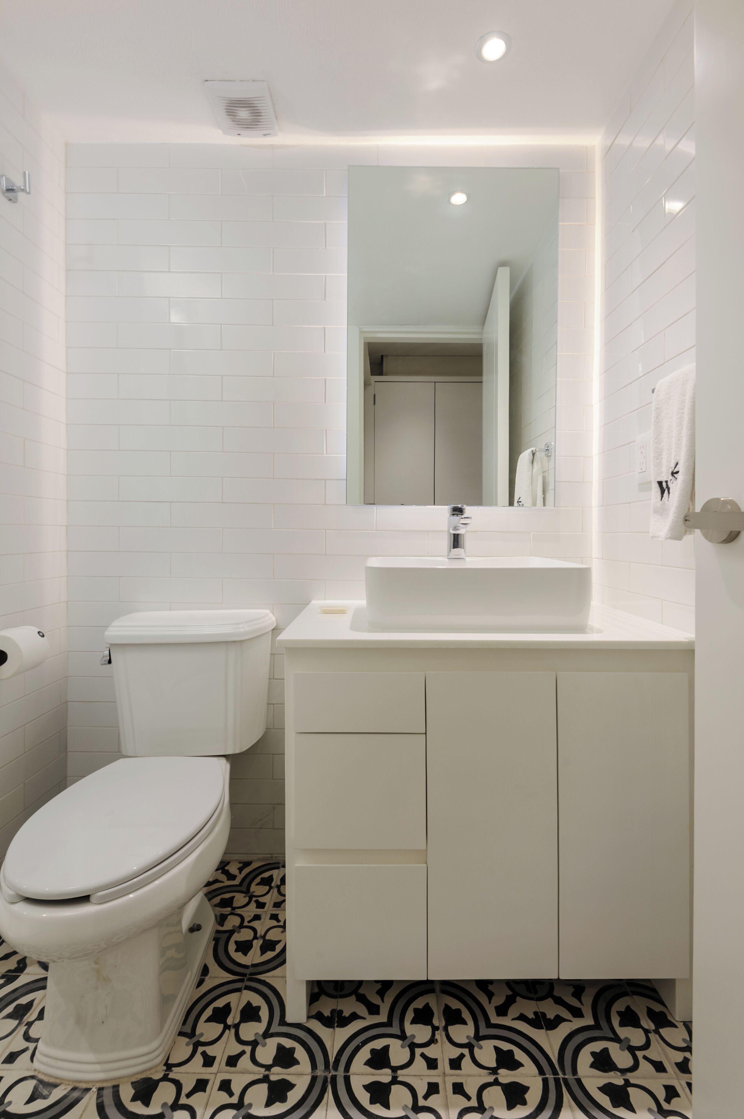Une salle de bain avec des toilettes, un lavabo et un miroir. Le sol est recouvert de carreaux formant un motif décoratif.