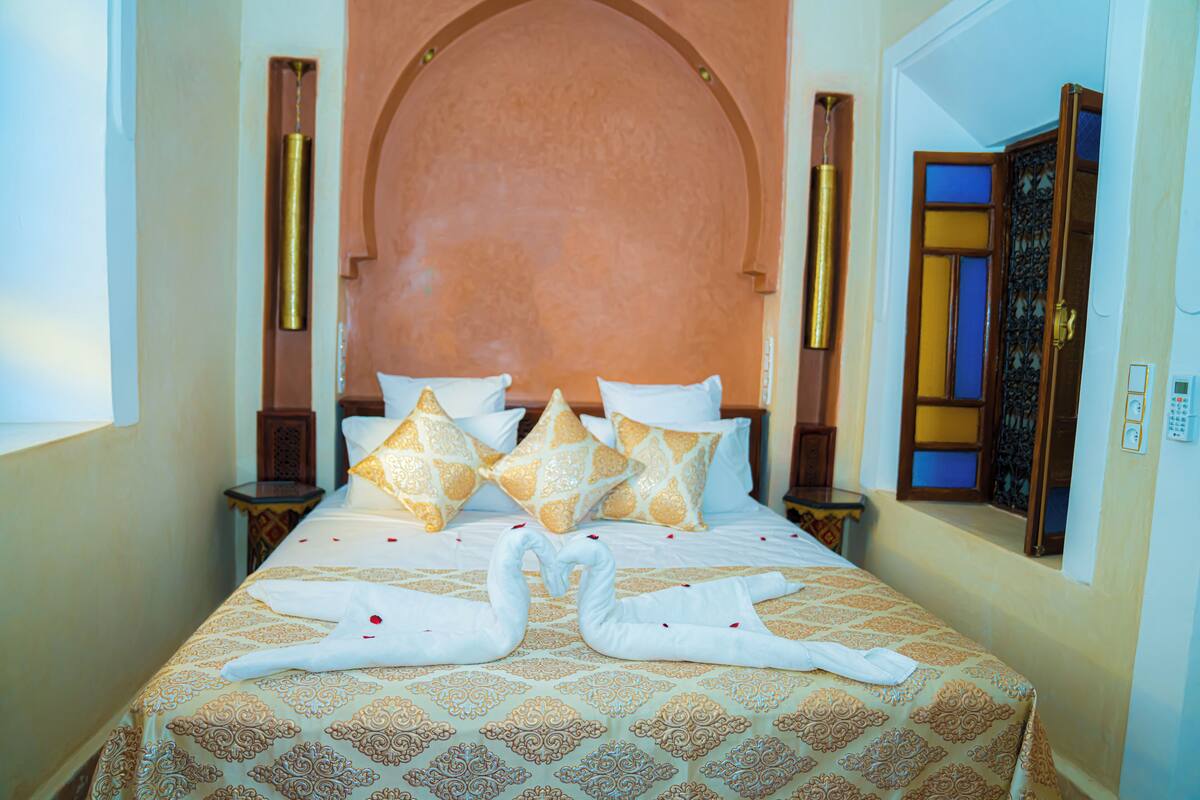 Quarto de hotel com uma cama grande, cabeceira elaborada e almofadas decorativas.