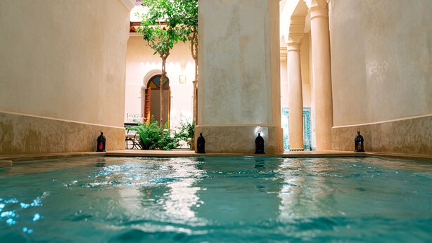 An indoor swimming pool with clear water, surrounded by arches and columns, and a tree in the background. - Riad Dar Zaouia (Marrakech)
