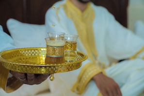 A tray with three glasses of a golden beverage, held by a person in a white robe with yellow trim. - Riad Dar Zaouia (Marrakech)