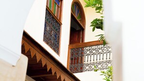 A narrow alleyway with a building featuring a wooden balcony with ornate metal railings and a window with a colorful geometric pattern. - Riad Dar Zaouia (Marrakech)