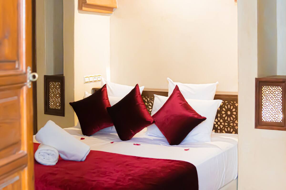 Quarto de hotel com uma cama grande, roupa de cama vermelha e uma porta de madeira.