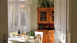 A dining area with a table set for two, a wooden cabinet with glass doors, and a potted plant. - Calm escape in historical athmosphere - Villa Giulietta Budapest,  free parking  (Budapest)