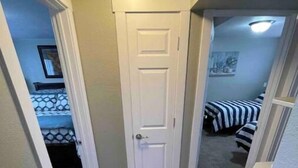 Un couloir avec un plancher en bois, une porte blanche et une chambre à coucher avec un lit et un tableau accroché au mur.