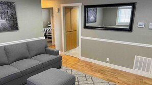 Un salon avec un canapé gris, un pouf gris et un tapis à motifs.