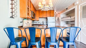 A kitchen with wooden cabinets, a white refrigerator, and a chandelier. There are four blue chairs around a wooden island. - Cozy Beach Condo Sleeps 6 POOL
 (Carolina Beach)