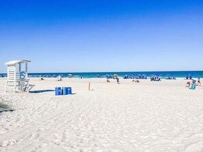 Una playa con una torre de salvavidas, sombrillas azules y cielos despejados.