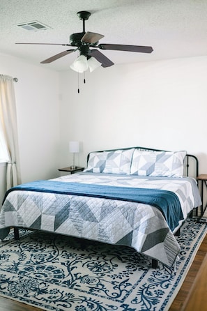 A bedroom with a bed, a ceiling fan, a nightstand, a lamp, and a patterned rug.
