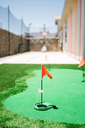 A miniature golf course with two flags, a green turf, and a stone wall in the background.