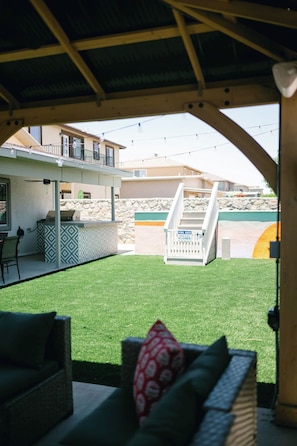 A covered outdoor seating area with a view of a pool and a stone wall.