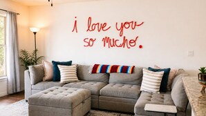 A living room with a sectional sofa, ottoman, and a wall with a red text message. - Family Retreat w/Pool - Golf - Pickleball Sleeps 9 (El Paso)