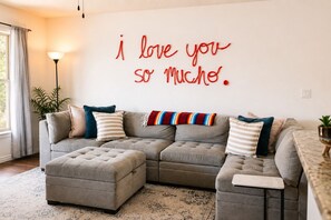A living room with a sectional sofa, ottoman, and a wall with a red text message. - Family Retreat w/Pool - Golf - Pickleball Sleeps 9 (El Paso)