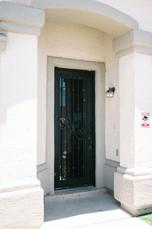 Una reja de metal negro con detalles decorativos, una puerta blanca y un letrero de advertencia sobre vigilancia con video las 24 horas.