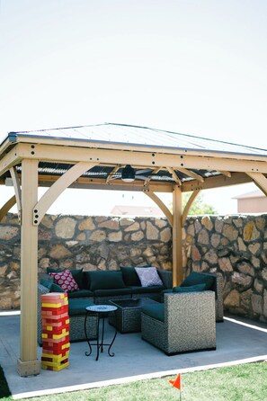 A covered outdoor seating area with a stone wall backdrop, a wooden pergola, and a jenga tower.