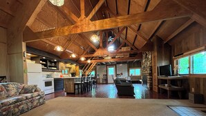 A spacious living area with a high ceiling and exposed wooden beams, a kitchen with a central island, and a cozy seating area with a fireplace. - Private, cozy cabin on 13 acres with two ponds (Bloomfield)