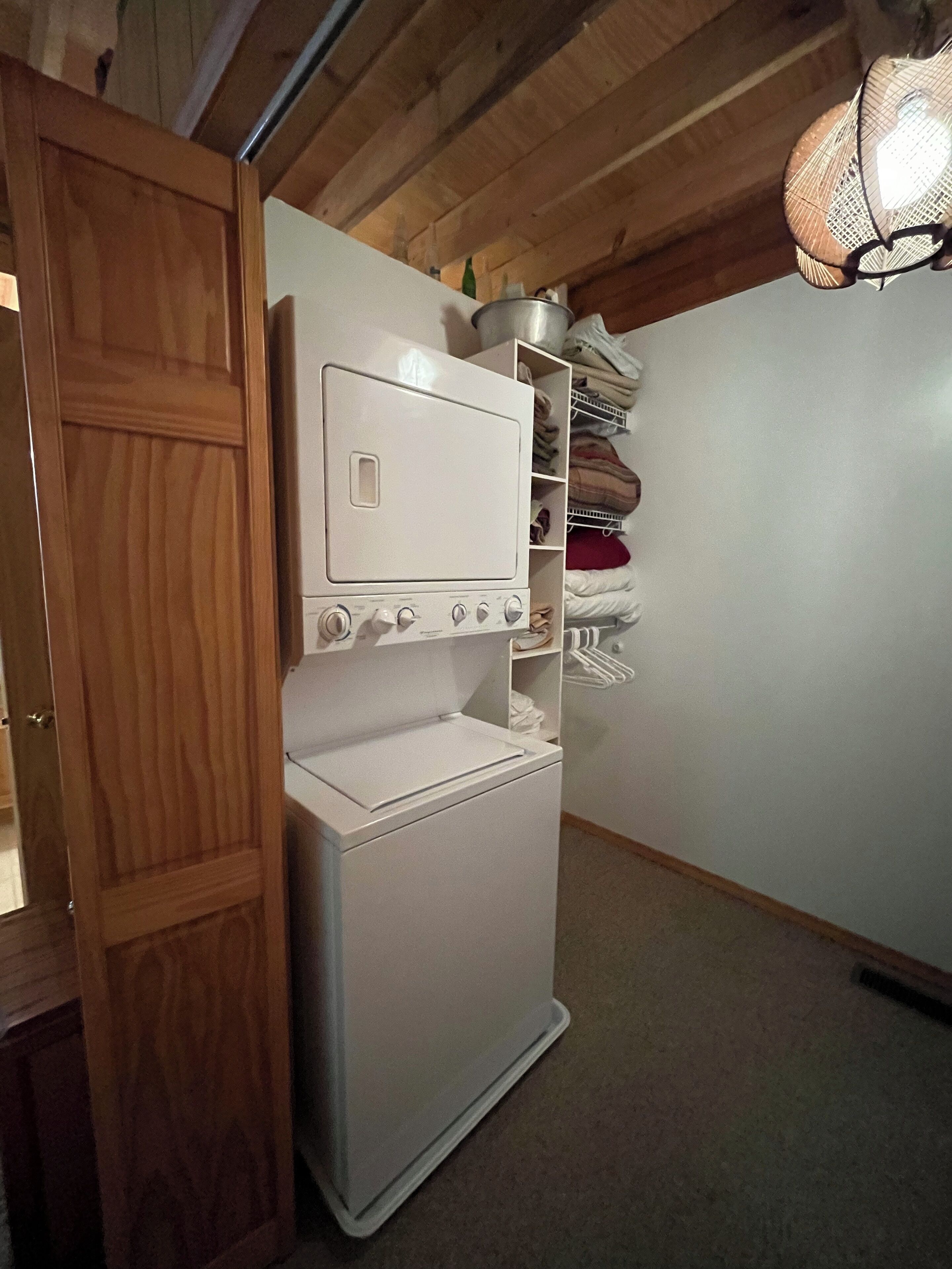 Une petite buanderie avec un lave-linge et un sèche-linge blancs, des poutres en bois au plafond et un étendoir suspendu.